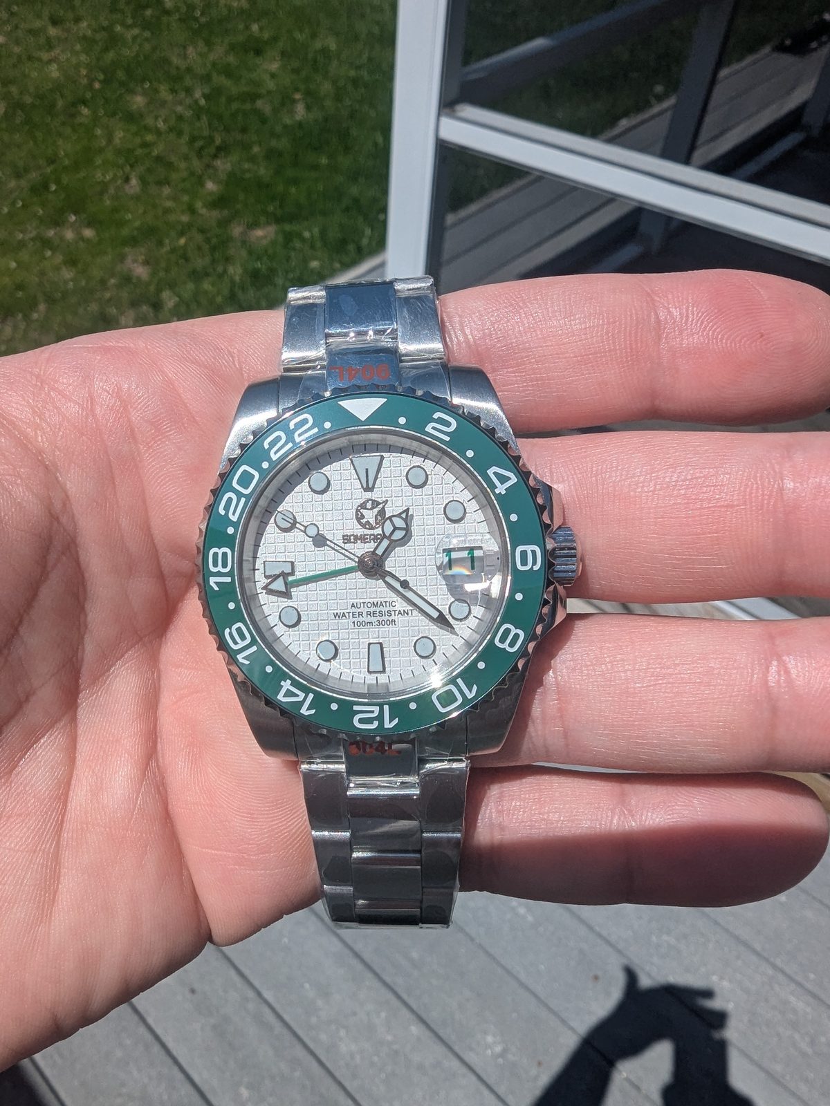 White dial GMT with green bezel held in palm